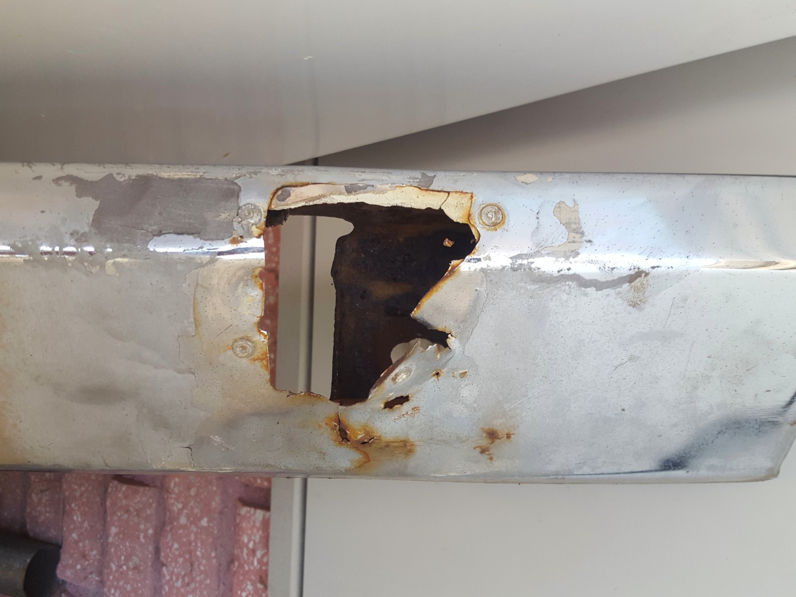 Någon har en gång i tiden försökt få loss kofångaren bak. Det har man gjort genom att såga hål i den! Bara för att komma på att där bakom sitter en korgmutter så den komemr man inte åt. Då har man popnita i en plåt och spacklat över det hela!